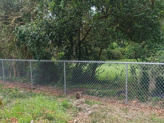 Una cerca de malla ciclónica galvanizada con riel superior y portón encerrando un lote arbolado en Florida