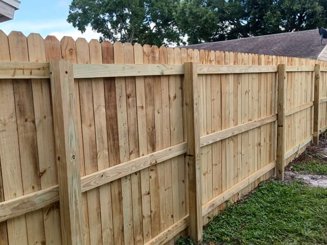 Una cerca alta de privacidad en madera con remate dog-ear construida por Marquez Yera Fence, con postes y travesaños a escuadra bajo el sol