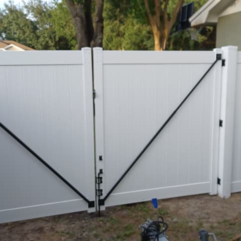 White vinyl double gate with diagonal braces, hung on a privacy fence beside a house