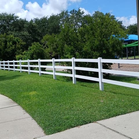 White vinyl ranch rail fence on a lawn beside a playground