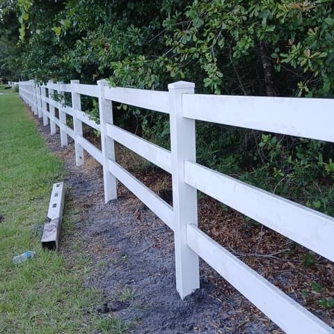 White vinyl ranch rail fence along a mulched bed, seen down its length