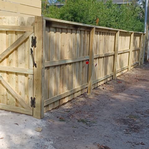 Wood gate braced diagonally and hung, the post footing still open beside a yellow house