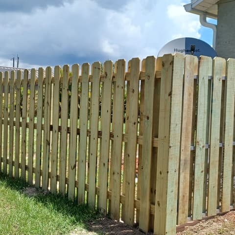 Wood shadowbox fence and gate following a house wall under a stormy sky